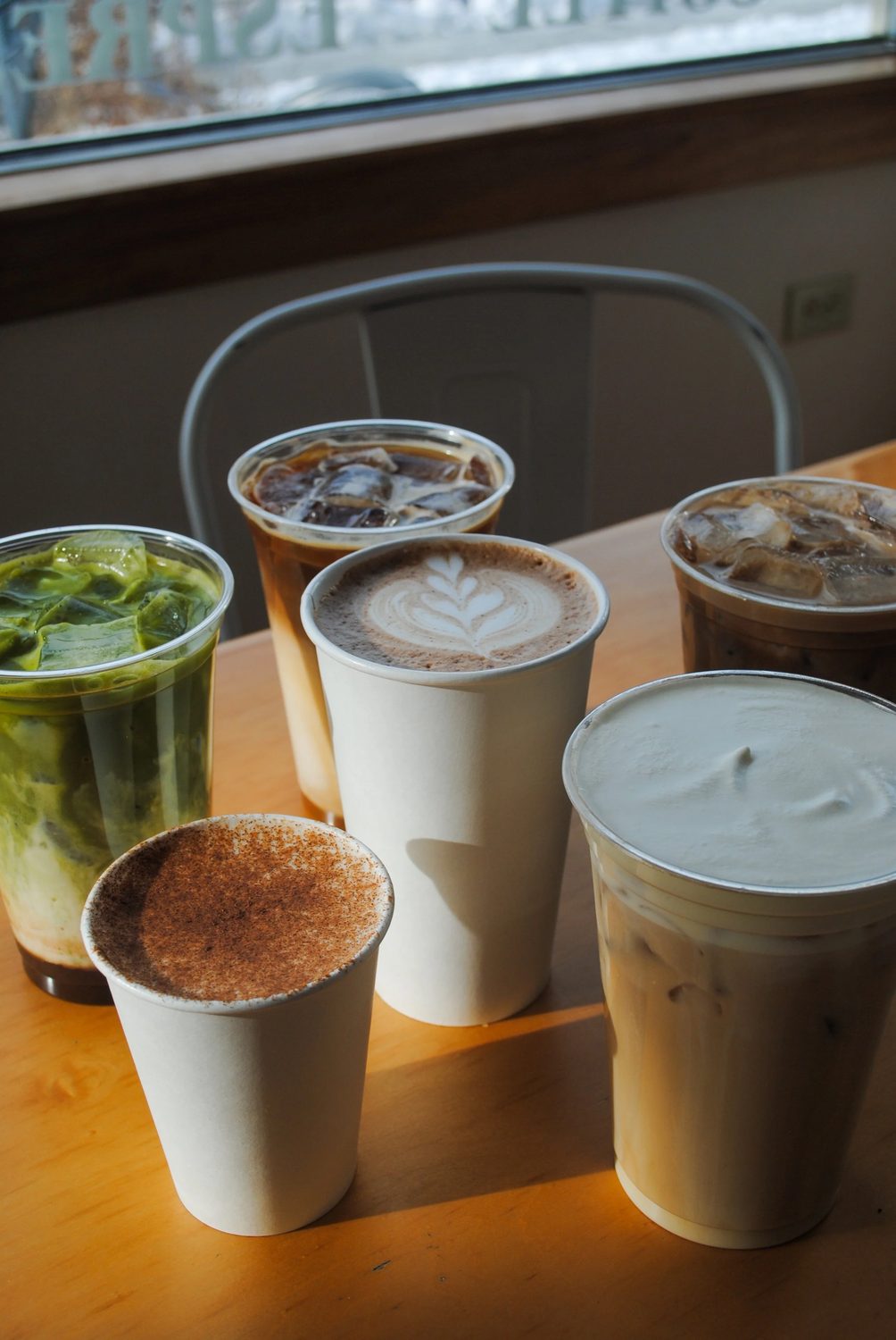 A row of coffees and iced drinks lined up along a sunny windowsill