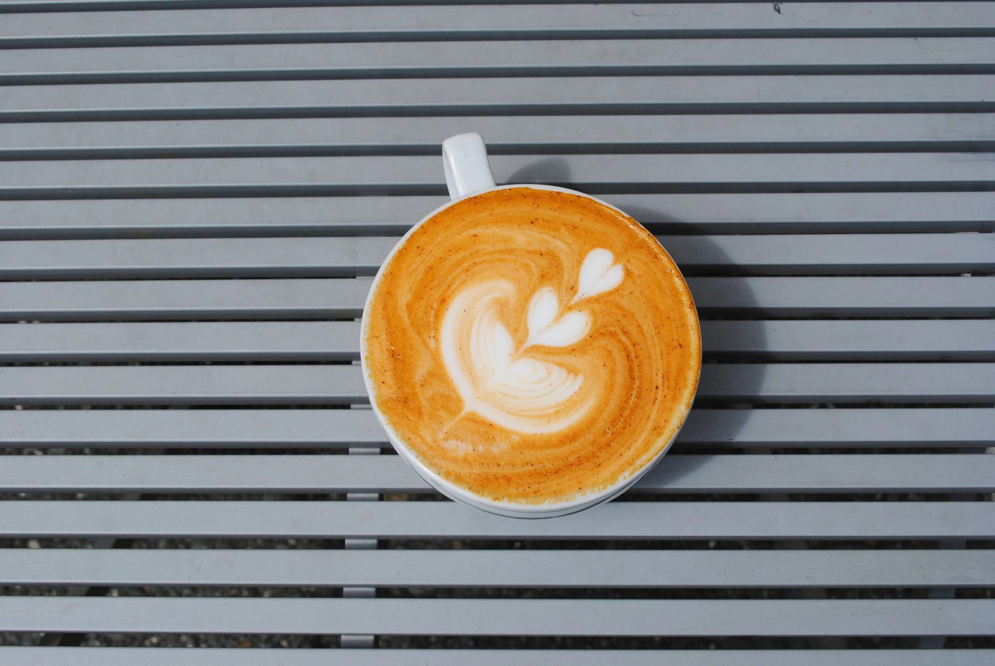 A latté with a leaf poured into the foam on a grey slatted table
