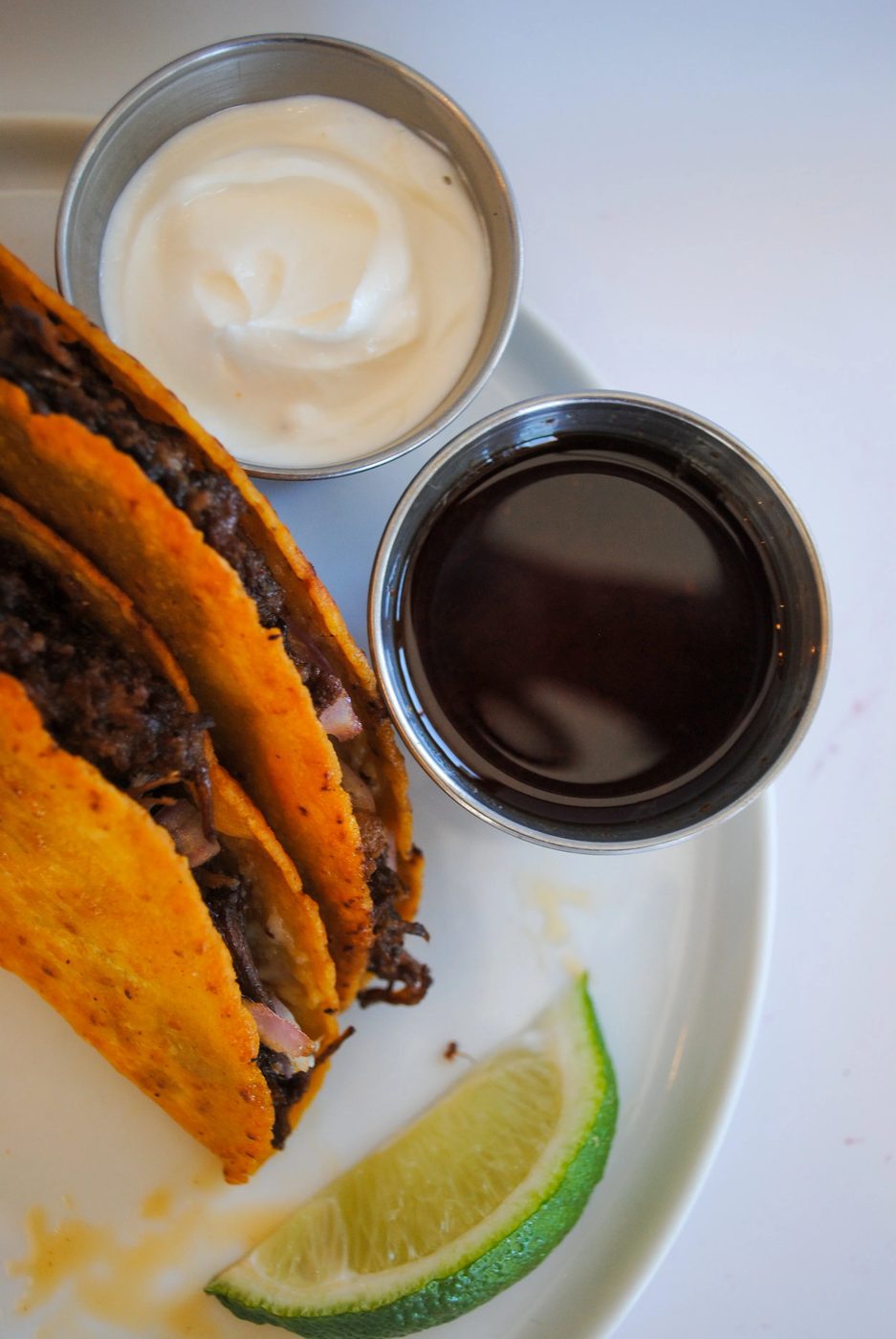 Two tacos and a cup of black coffee on a plate with a lime wedge